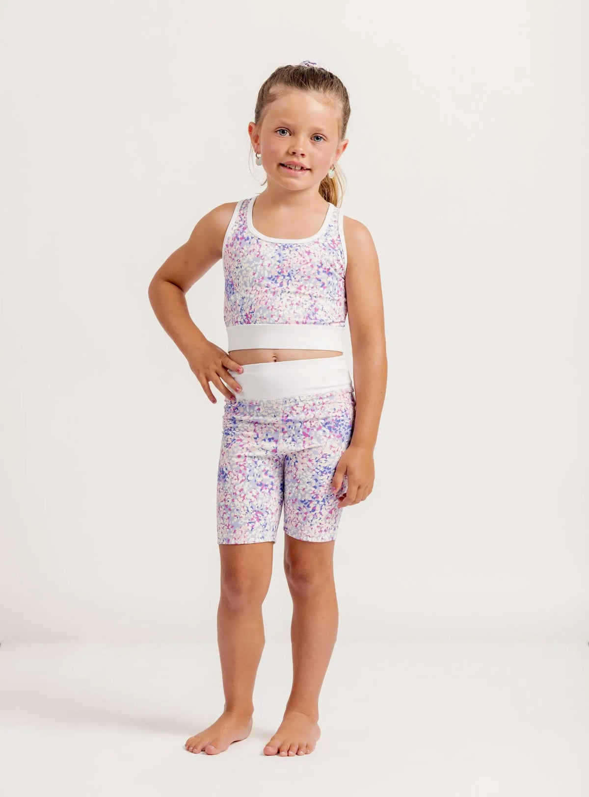 Young girl wearing a colorful sports crop and shorts set on a white background