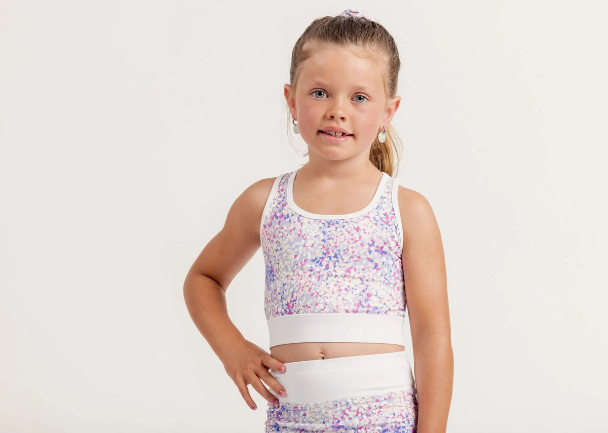 Young girl wearing a colorful top and white pants on a light background