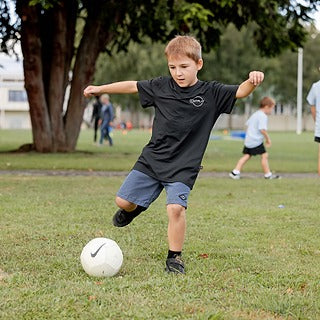Young boy kicking soccer ball in a field, wearing Outplay black T shirt
