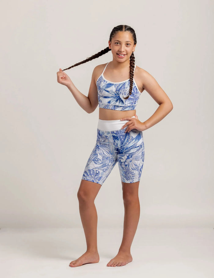 Girl wearing a Fearless Blue Monstera patterned crop and Get Moving Bike Shorts on a plain background
