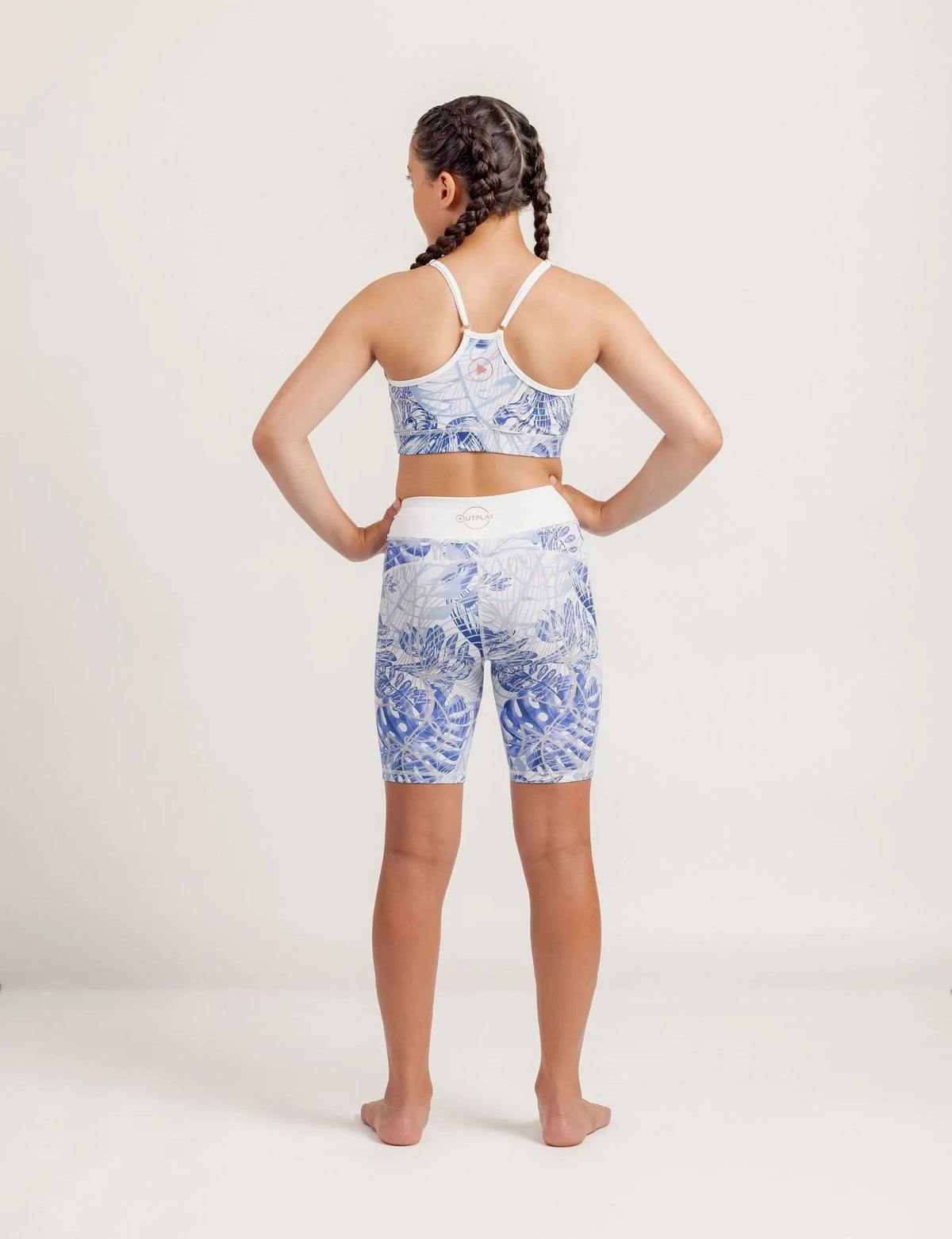 Girl wearing a Fearless Blue Monstera patterned crop and Get Moving Bike Shorts on a plain background