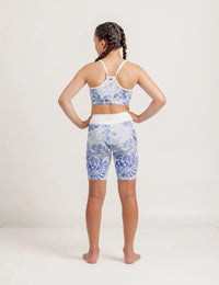 Girl wearing a Fearless Blue Monstera patterned crop and Get Moving Bike Shorts on a plain background