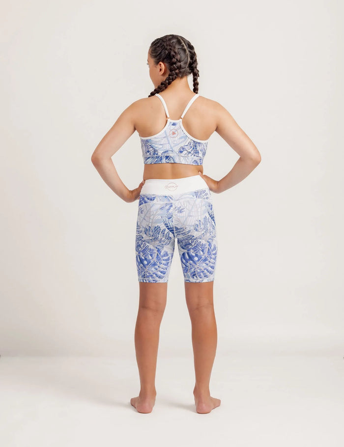 Girl wearing a Fearless Blue Monstera patterned crop and Get Moving Bike Shorts on a plain background