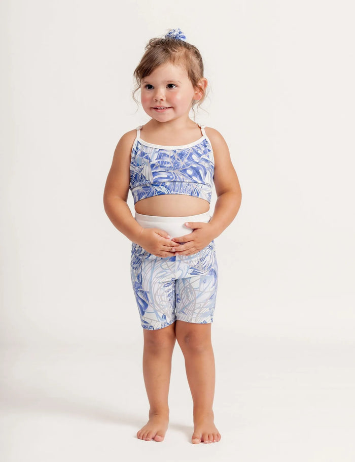 Girl wearing a Fearless Blue Monstera patterned crop and Get moving bike shorts on a plain background