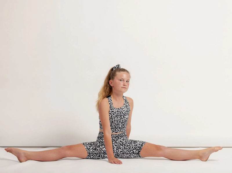 Girl in an Ignite Snow Leapord Crop top and Get moving bike shorts performing a split on a light background 
