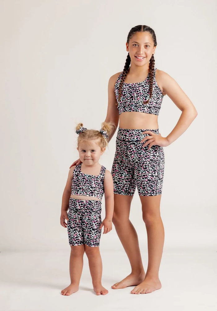 Two girls wearing Envy Me Multi coloured leopard print crop and bike shorts sets on a white background