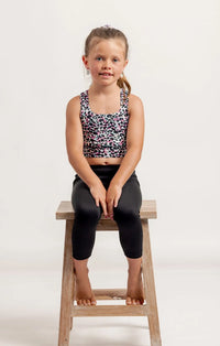 Young girl sat on a wooden stool, wearing a Multi coloured leopard print crop top and black Go Get Em 3/4 leggings on a white background