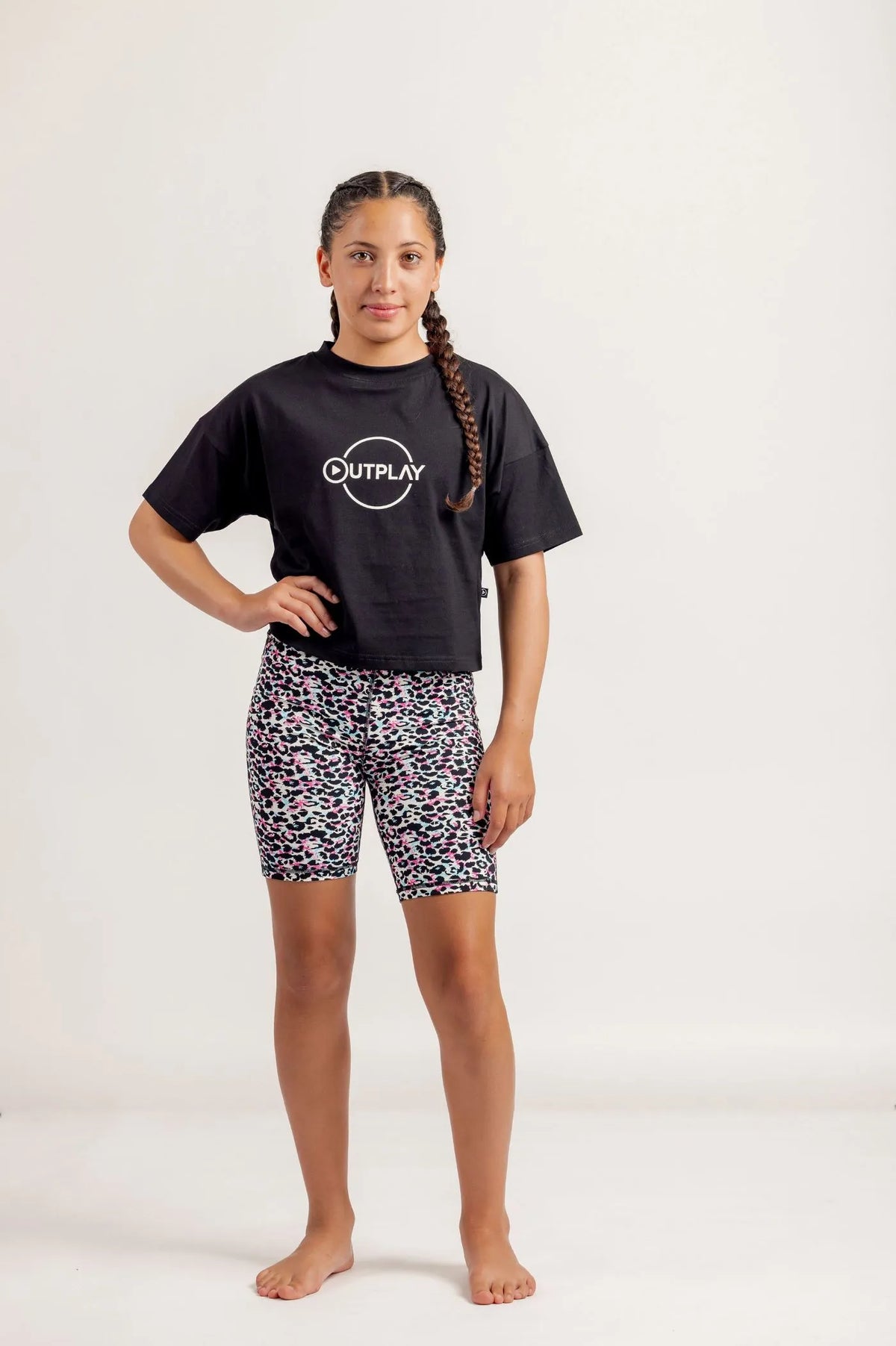 Girl wearing Black crop Tshirt and multicoloured bike shorts on a light background