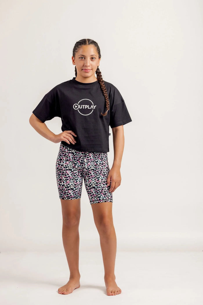 Girl wearing Black crop Tshirt and multicoloured bike shorts on a light background