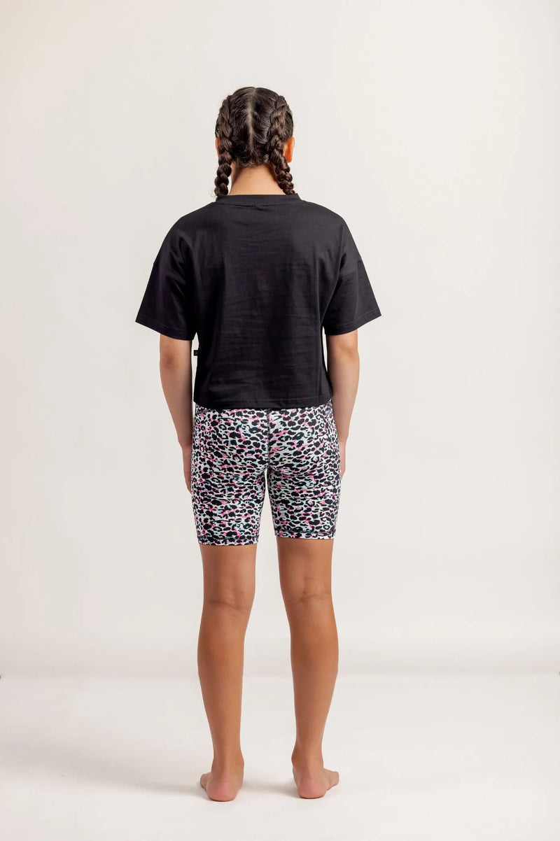 Girl wearing Black crop Tshirt and multicoloured bike shorts on a light background