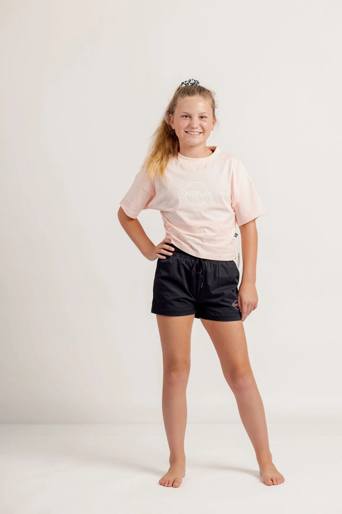 Girl wearing a light pink crop Tshirt and black shorts on a light background