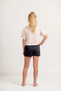 Girl wearing a light pink crop Tshirt and black shorts on a light background