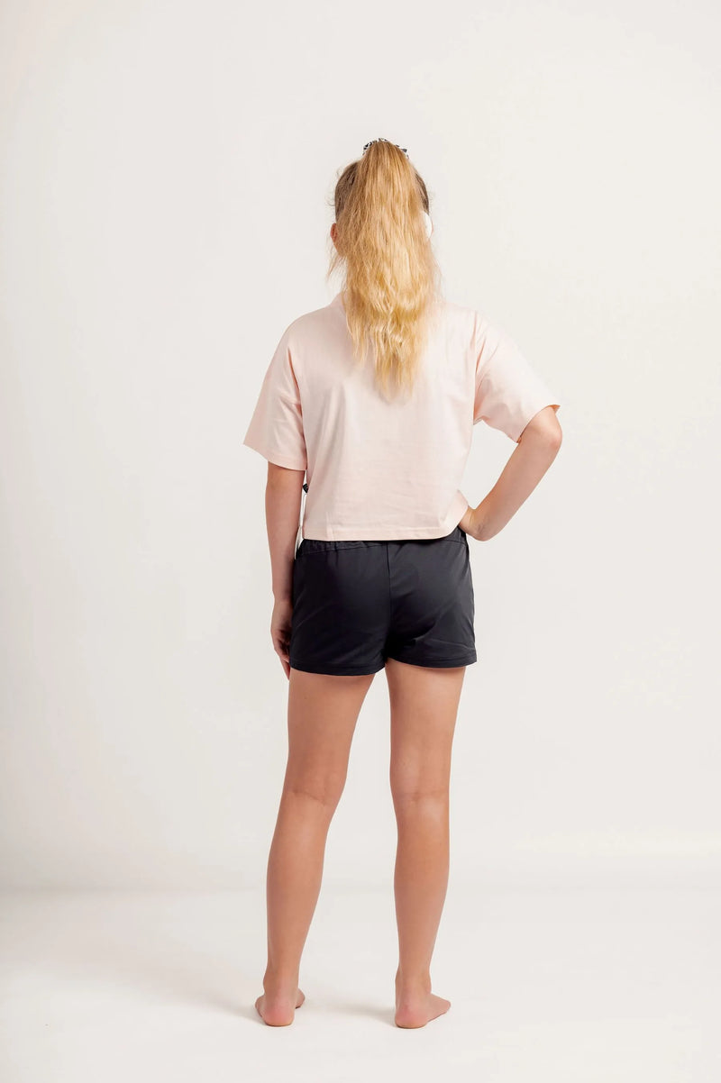 Girl wearing a light pink crop Tshirt and black shorts on a light background