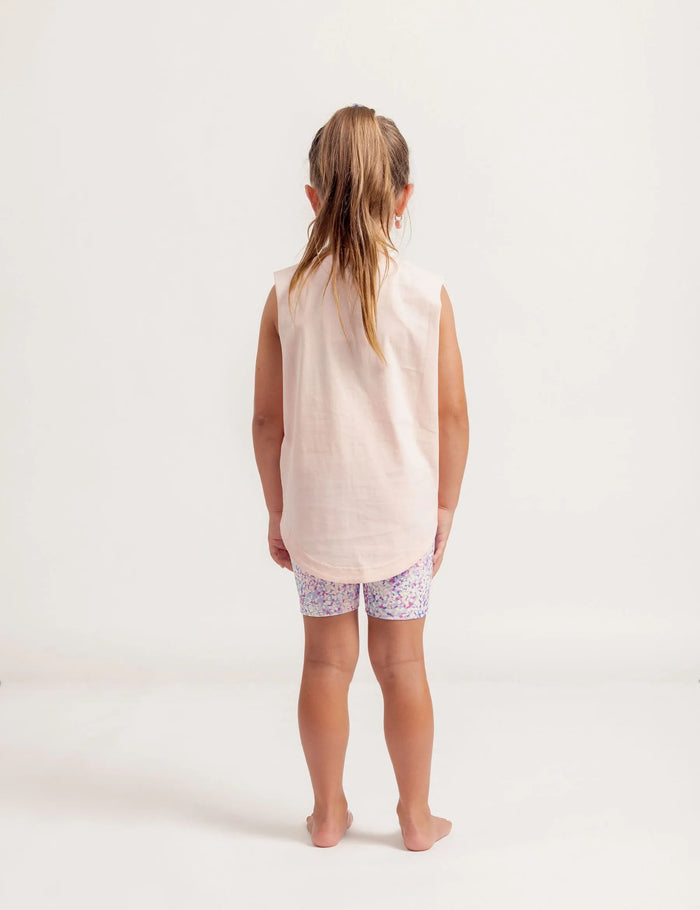 Young girl wearing a Shine Bright sleeveless top and patterned shorts on a white background