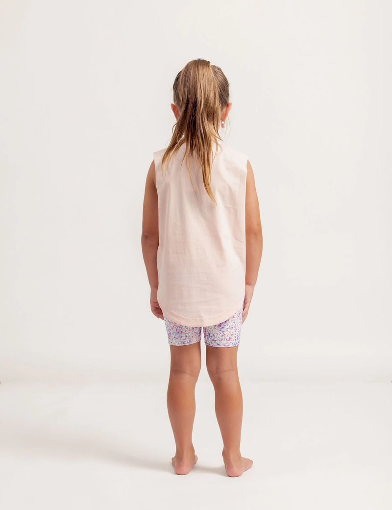Young girl wearing a Shine Bright sleeveless top and patterned shorts on a white background