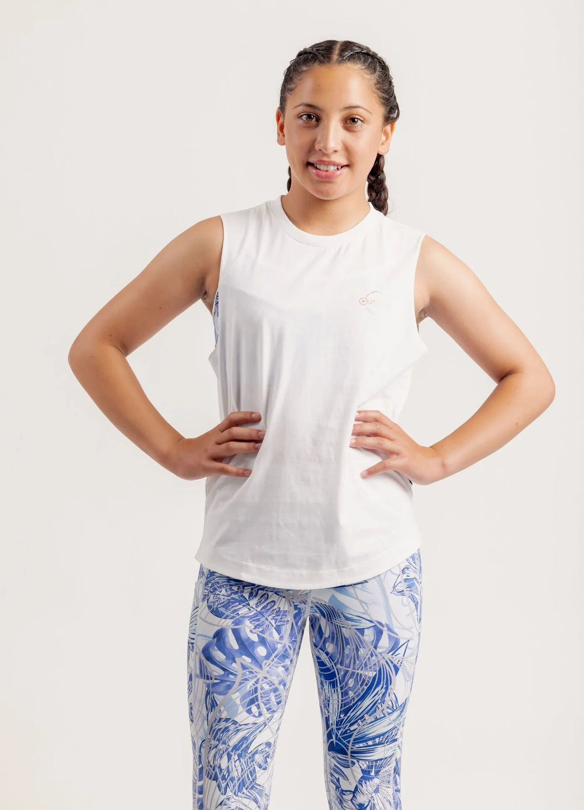 Girl wearing a Shine Bright white sleeveless top and Limitless Blue Monstera patterned leggings on a white background