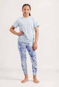 Girl wearing a light blue t-shirt and Blue Monstera Limitless leggings on a white background