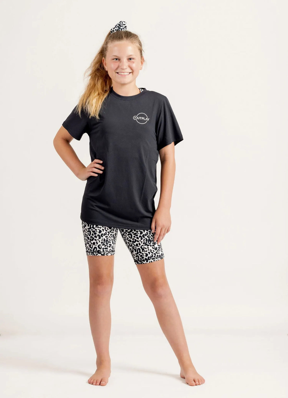 Young girl wearing a Gametime black t-shirt and Ignite Snow Leopard patterned bike shorts on a white background