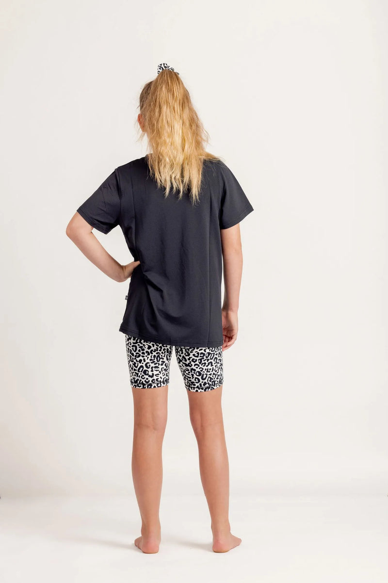 Girl wearing a Gametime black t-shirt and Ignite Snow Leopard patterned bike shorts on a white background