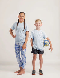 Two children wearing Gametime light blue shirts and patterned pants on a white background